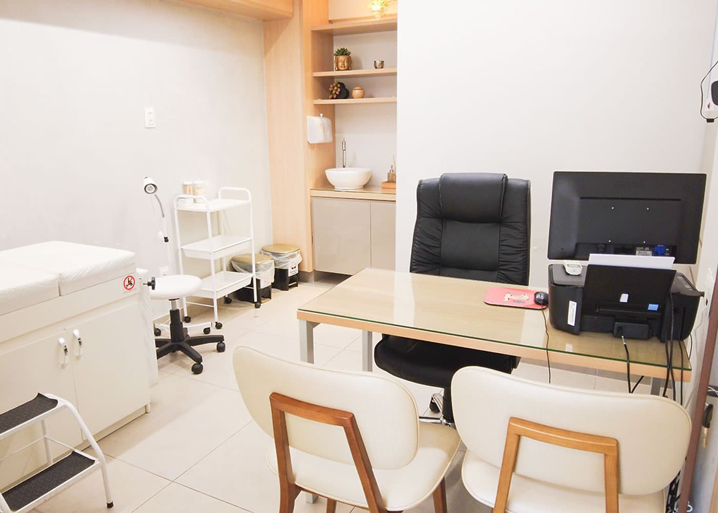 Sala de atendimento da unidade Prado do Instituto Hiraki com maca, pia, carrinho auxiliar e mesa com computador