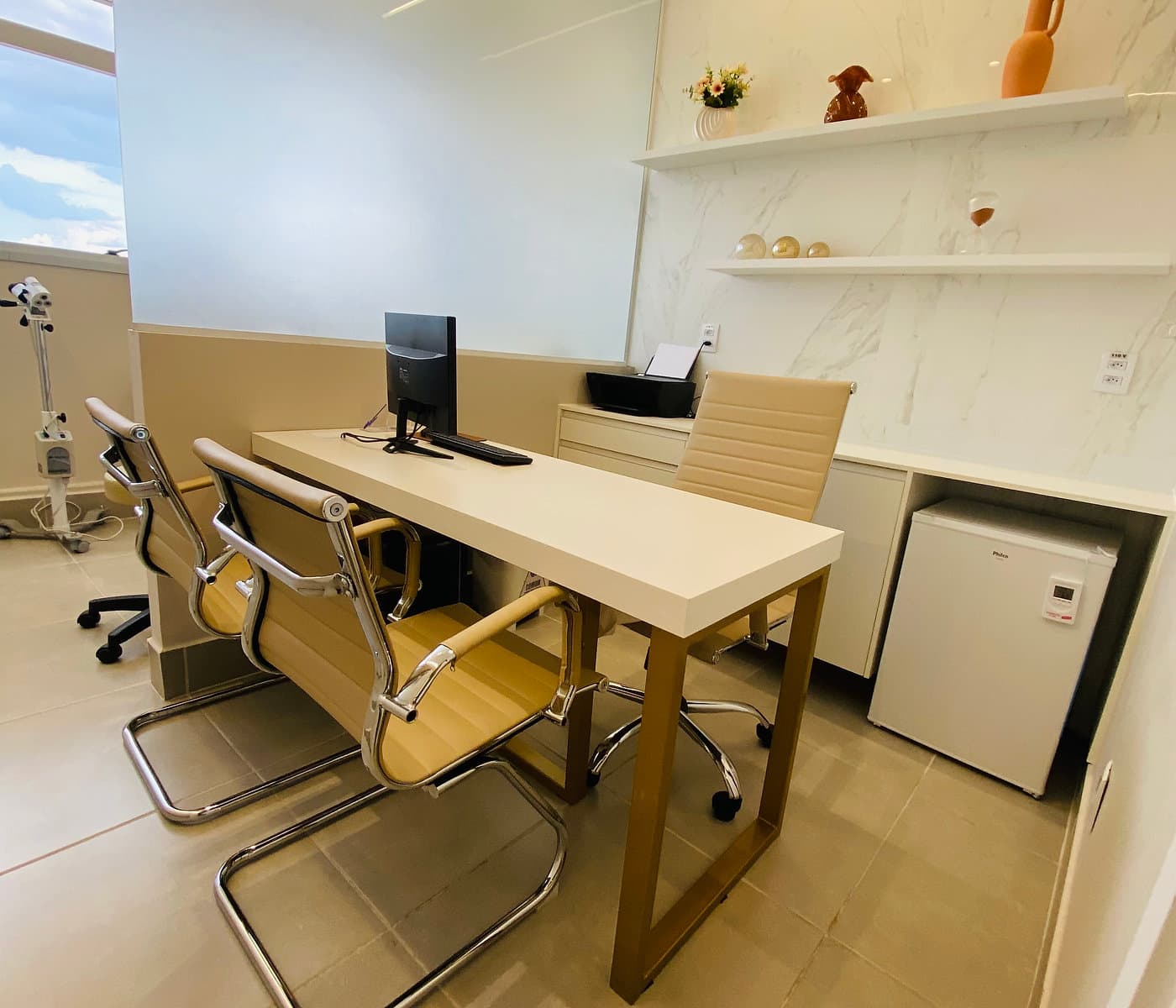 Consultório da unidade Lourdes do Instituto Hiraki com mesa de atendimento, cadeiras, frigobar e foco clínico