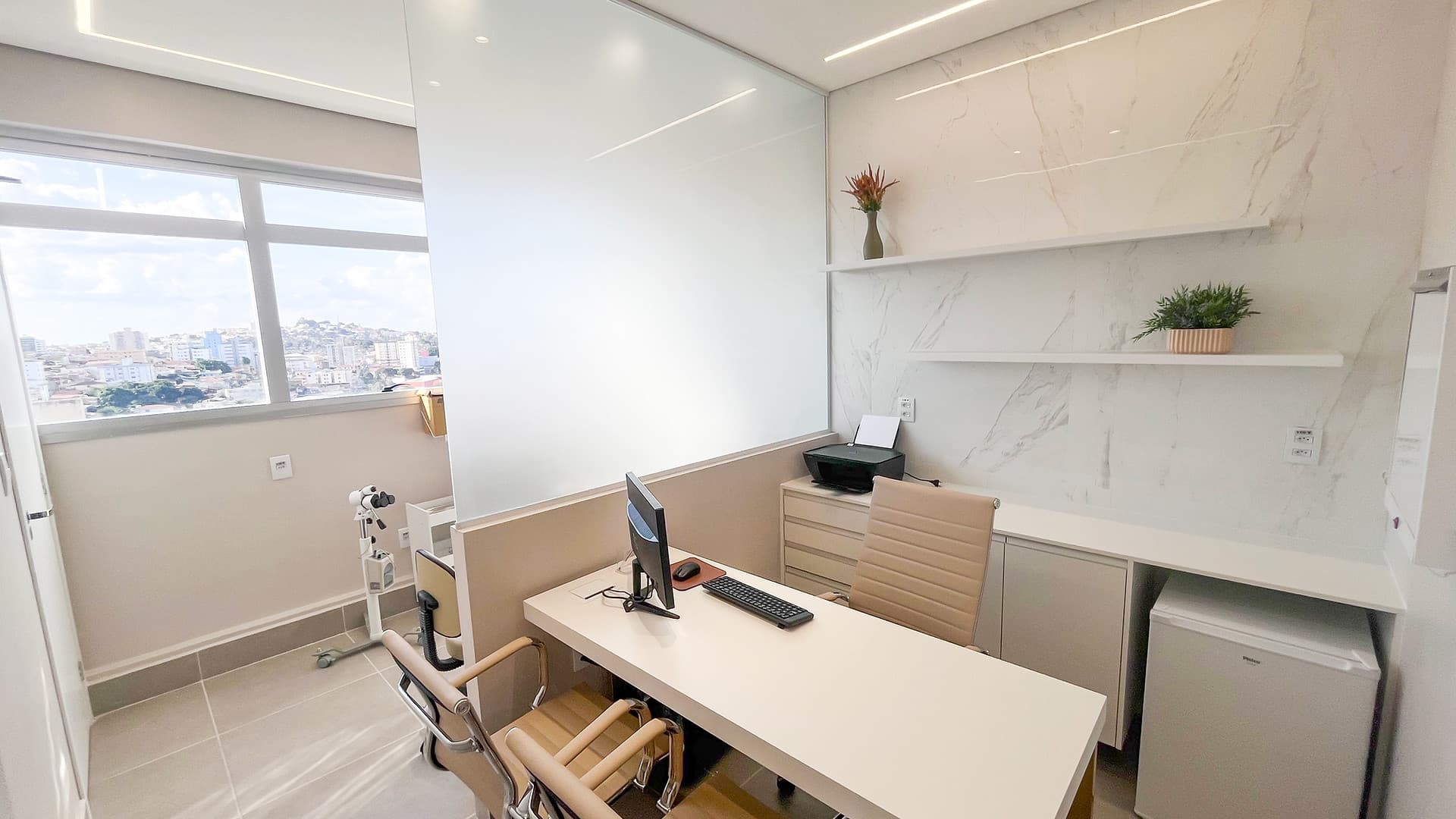 Consultório da unidade Lourdes do Instituto Hiraki com mesa branca, cadeiras e janela com vista para Belo Horizonte