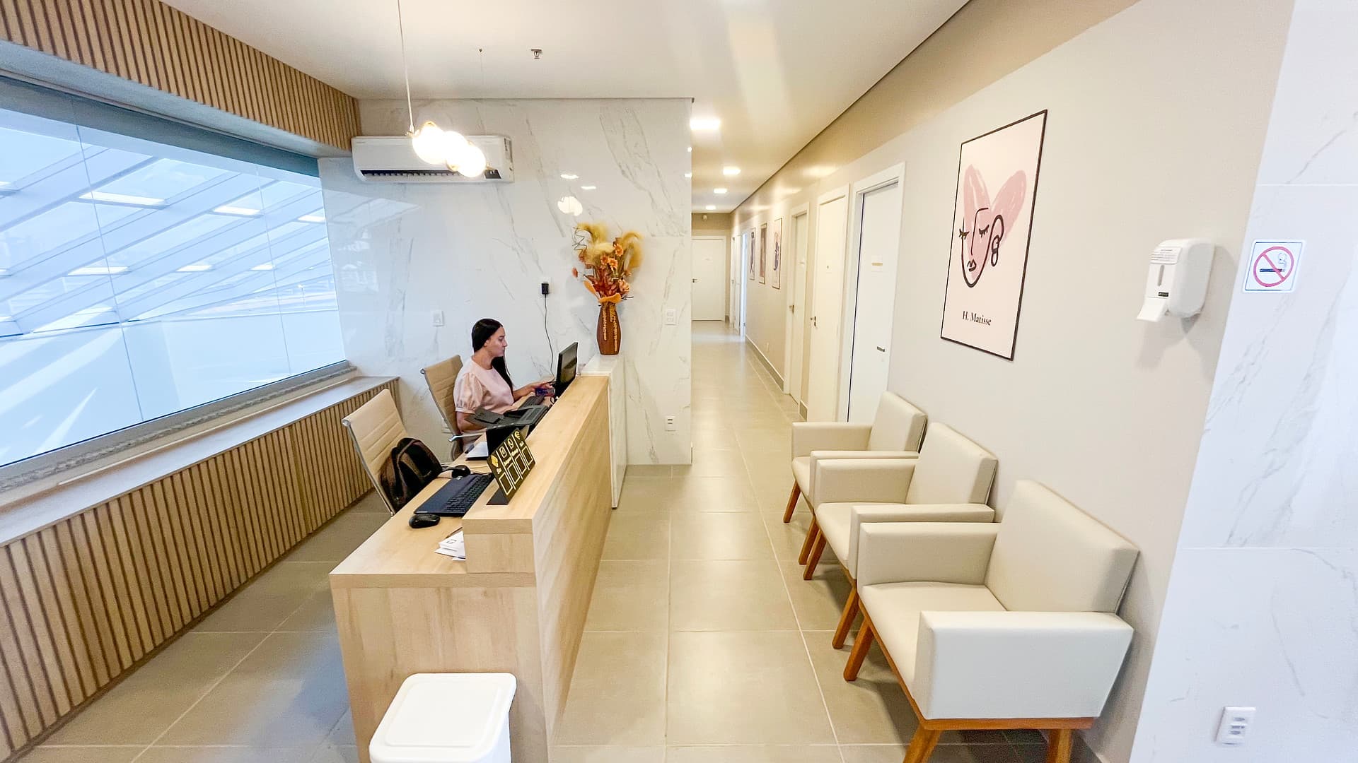 Recepção e corredor das salas da unidade Lourdes do Instituto Hiraki, com balcão de madeira e poltronas de espera